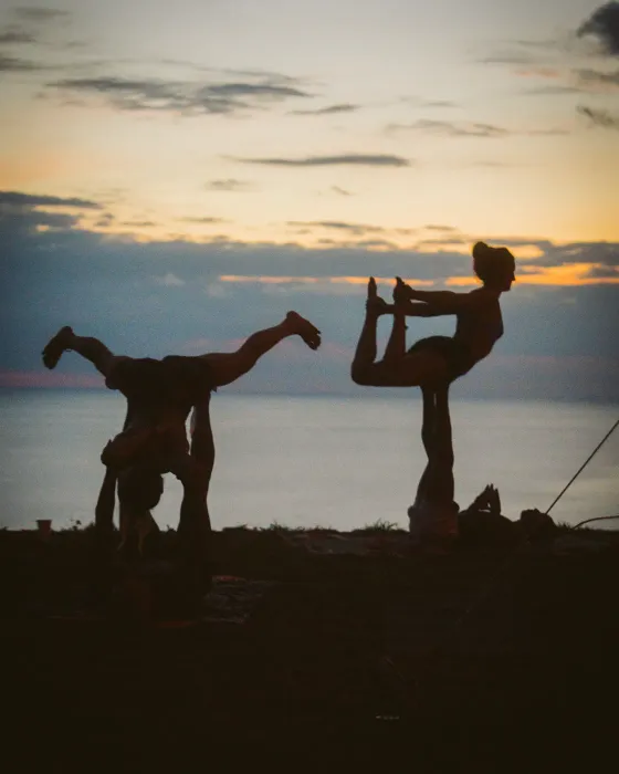 Two acro pairs balancing in silhouette at Amora against the last of the light over the Pacific.