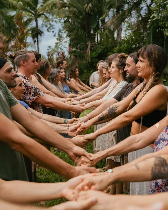 Two facing rows of people reaching out to clasp each other's hands on the grass at a village gathering at Amora, Costa Rica.