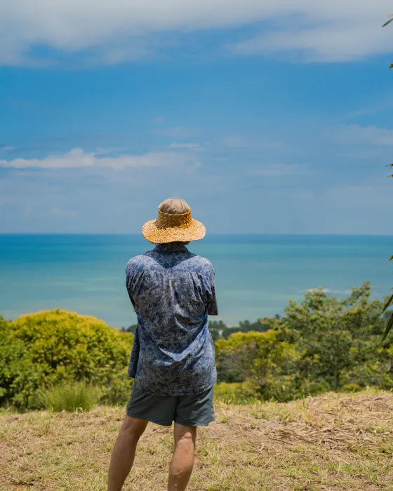 A man in a woven hat standing on the ocean-view ridge at Amora, looking out over the turquoise sea of the Costa Ballena.