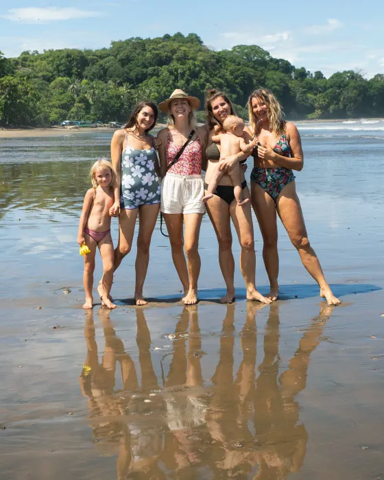 Four women with a baby and a small girl on the wet sand at low tide, mirrored in the water, at the beach below Amora near Dominical.