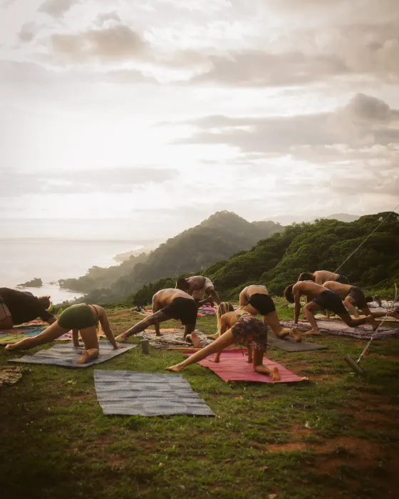 A morning yoga session on the land at Amora, the community on mats spread over the ridge grass with the Costa Ballena coastline pale below — an ocean-view ecovillage in Costa Rica.